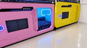 Una estructura en forma de cápsula de color rosa y amarillo con un panel de control y una cama en su interior.