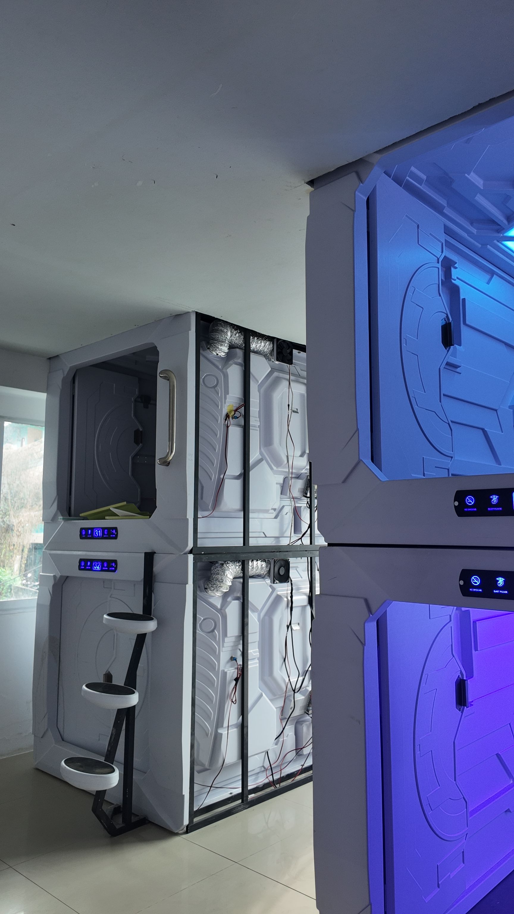 A modern room with a large, white, wall-mounted unit featuring a digital display and control panel, and a smaller, blue-lit unit with a control panel.