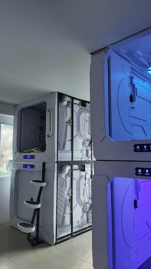 A modern room with a large, white, wall-mounted unit featuring a digital display and control panel, and a smaller, blue-lit unit with a control panel.