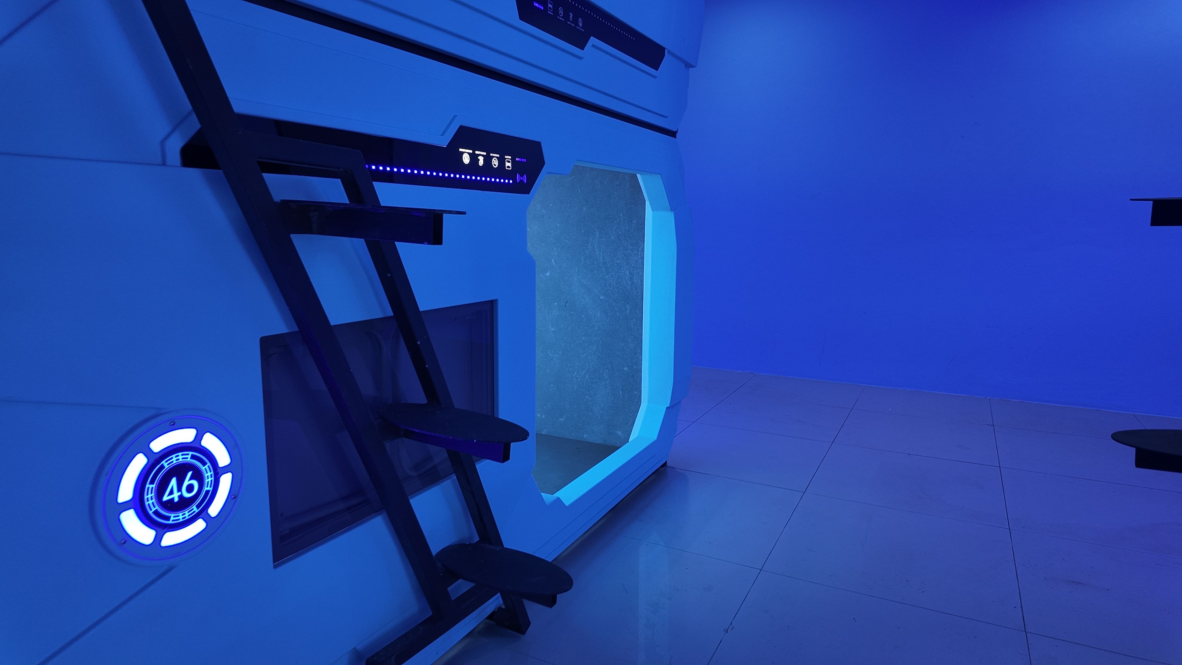 Une pièce avec un mur éclairé en bleu, une échelle et un écran numérique.