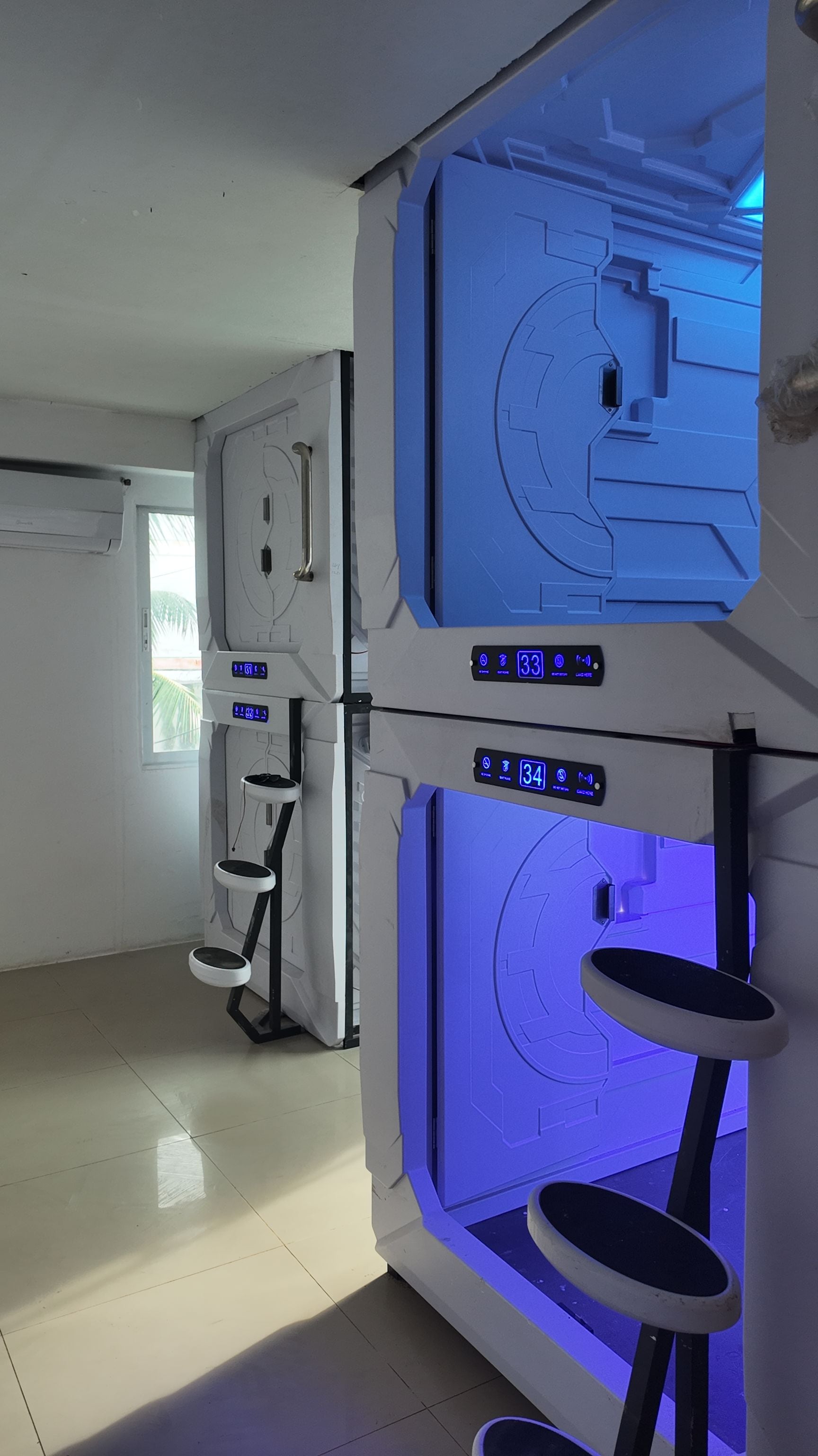 A room with a large blue machine, two digital displays, and a window with a view of palm trees.