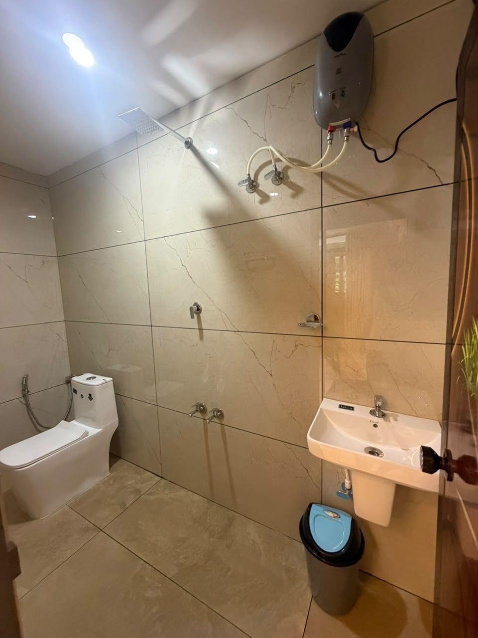 Un baño con inodoro, lavamanos, ducha y un cubo de basura.