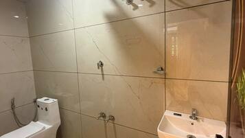 Un baño con inodoro, lavamanos, ducha y un cubo de basura.