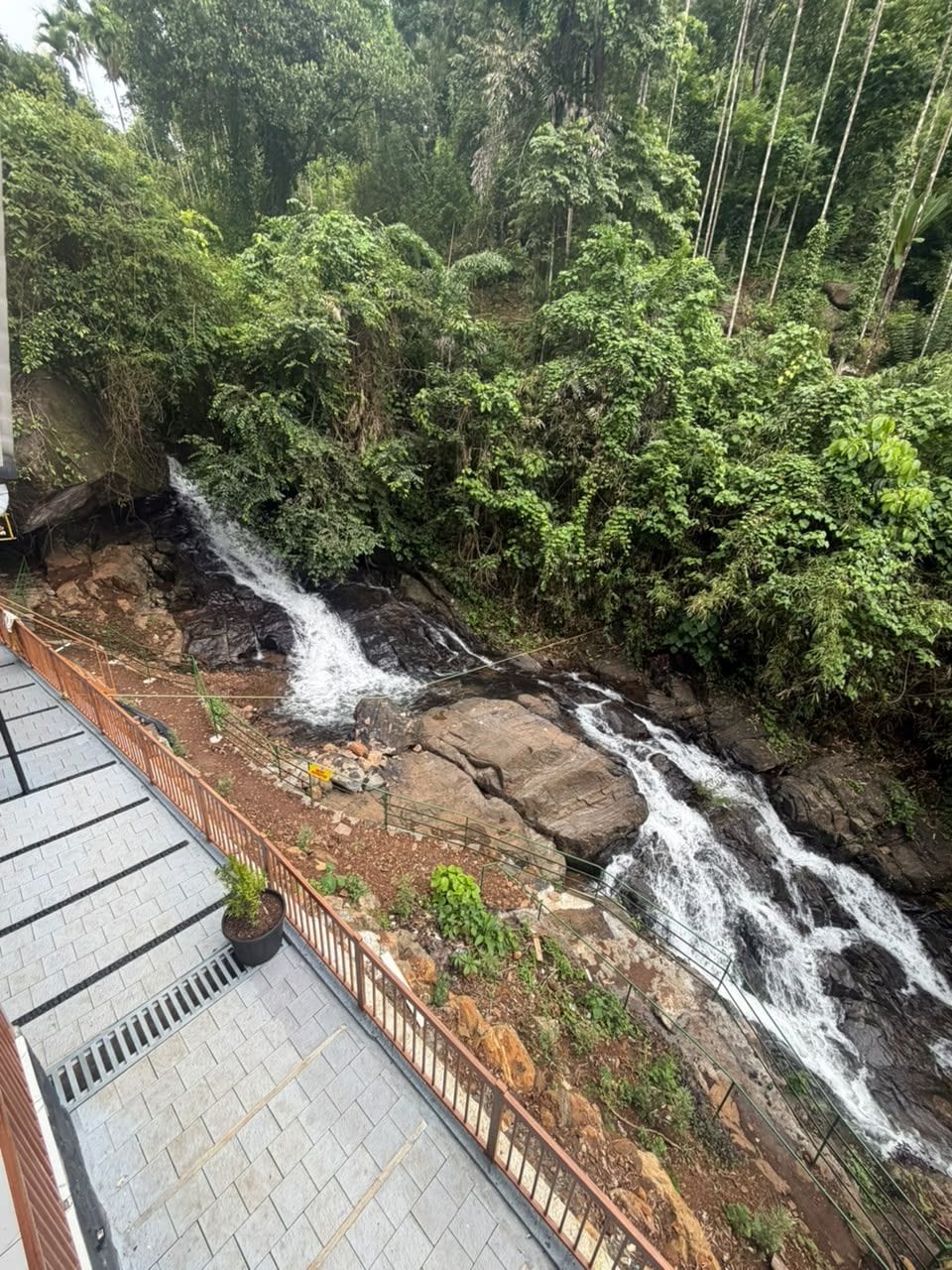 A waterfall cascading over rocks with a paved walkway and a metal railing.
