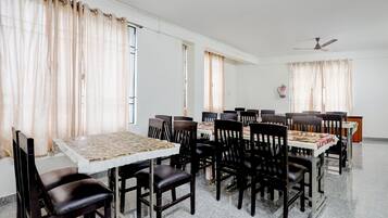 A dining area with multiple tables and chairs, a ceiling fan, and windows with curtains.
