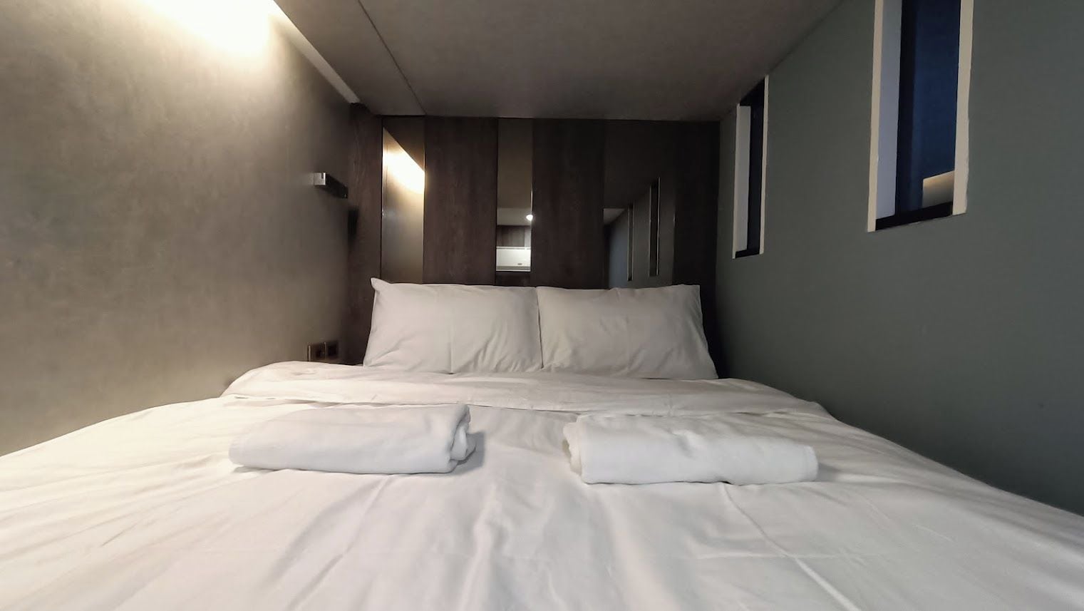 A hotel room with a neatly made bed, a mirror, and a window.