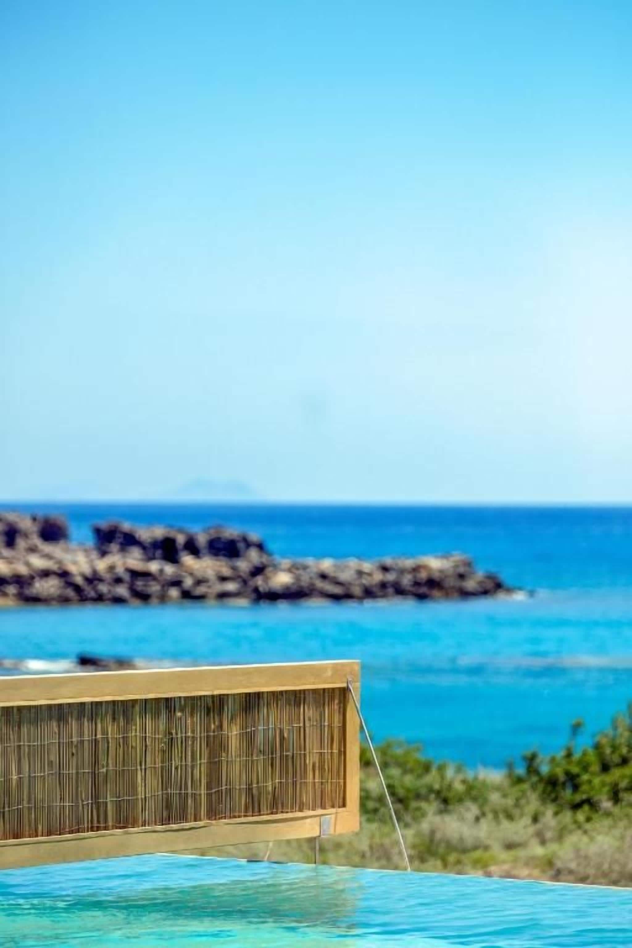 A pool with a bamboo barrier and a view of the ocean and rocky coastline.