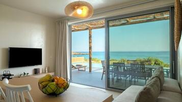 A modern living room with a flat-screen TV, a dining table with a fruit bowl, and a sofa.