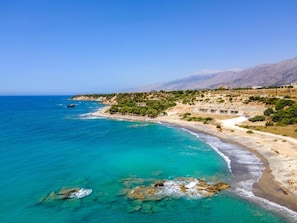 Un paisaje costero con una playa, aguas turquesas cristalinas y montañas al fondo.
