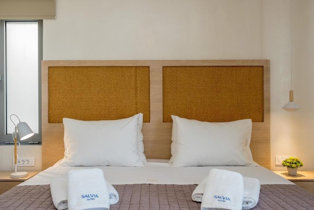 A double bed with a headboard, two pillows, a blanket, and two towels with the brand name 'SALVIA' on them.