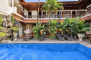 A swimming pool with a tiled deck, surrounded by potted plants and a stone wall.
