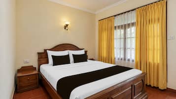 Habitación de hotel con cama de madera, mesita de noche, lámpara de pared y ventana con cortinas amarillas.