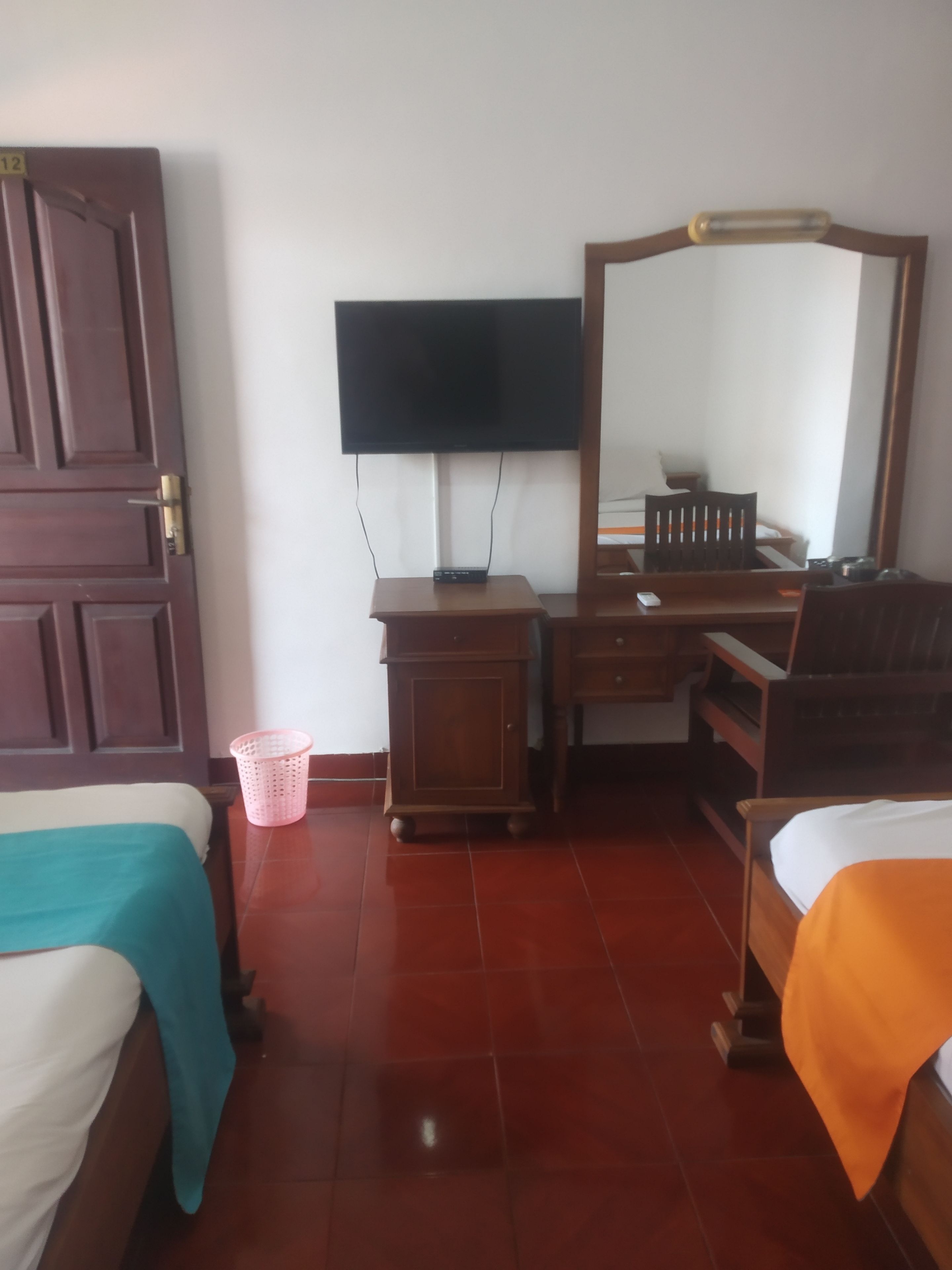 A hotel room with two beds, a desk with a television, a mirror, and a small trash bin.