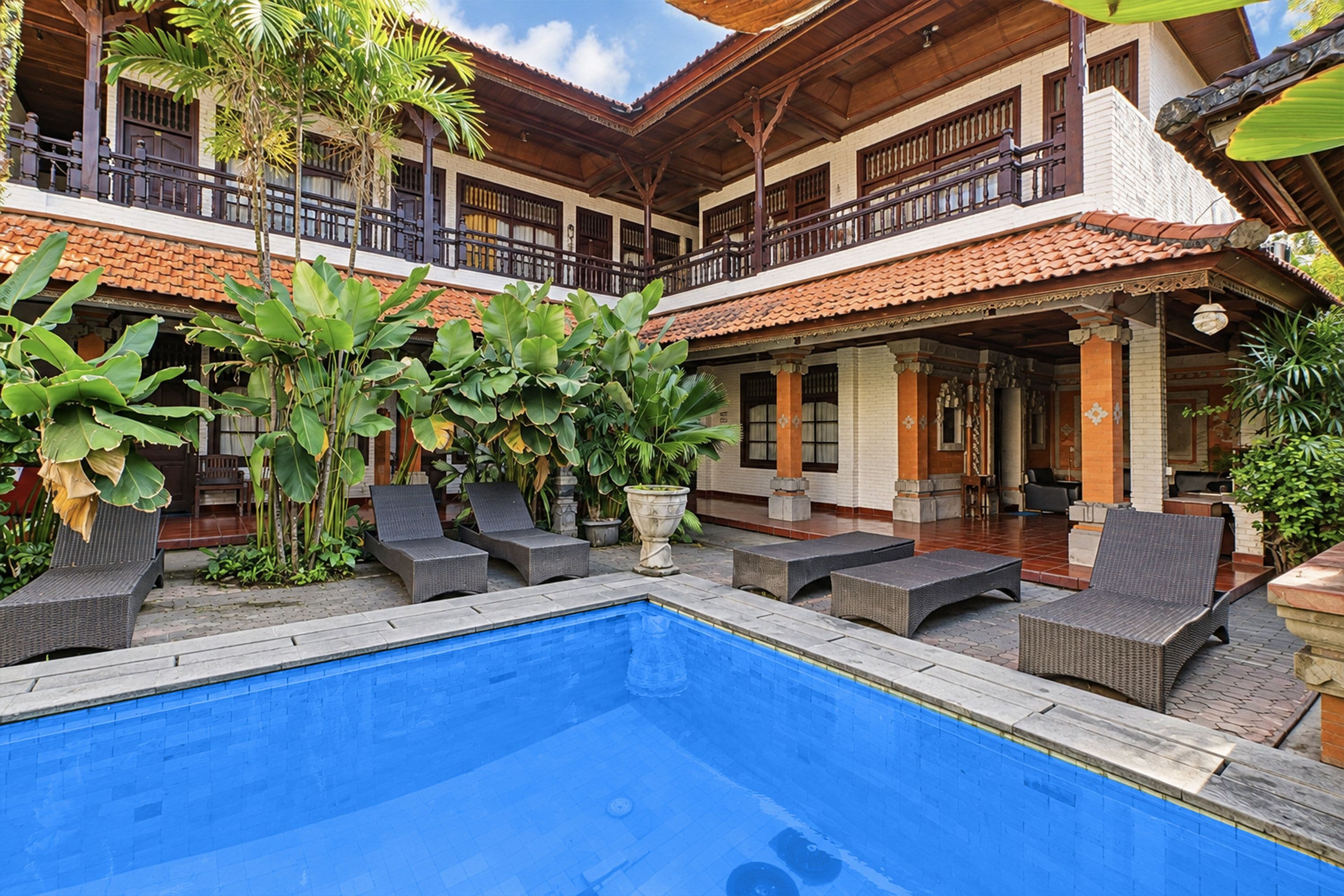 A pool area with lounge chairs and a two-story building with balconies.