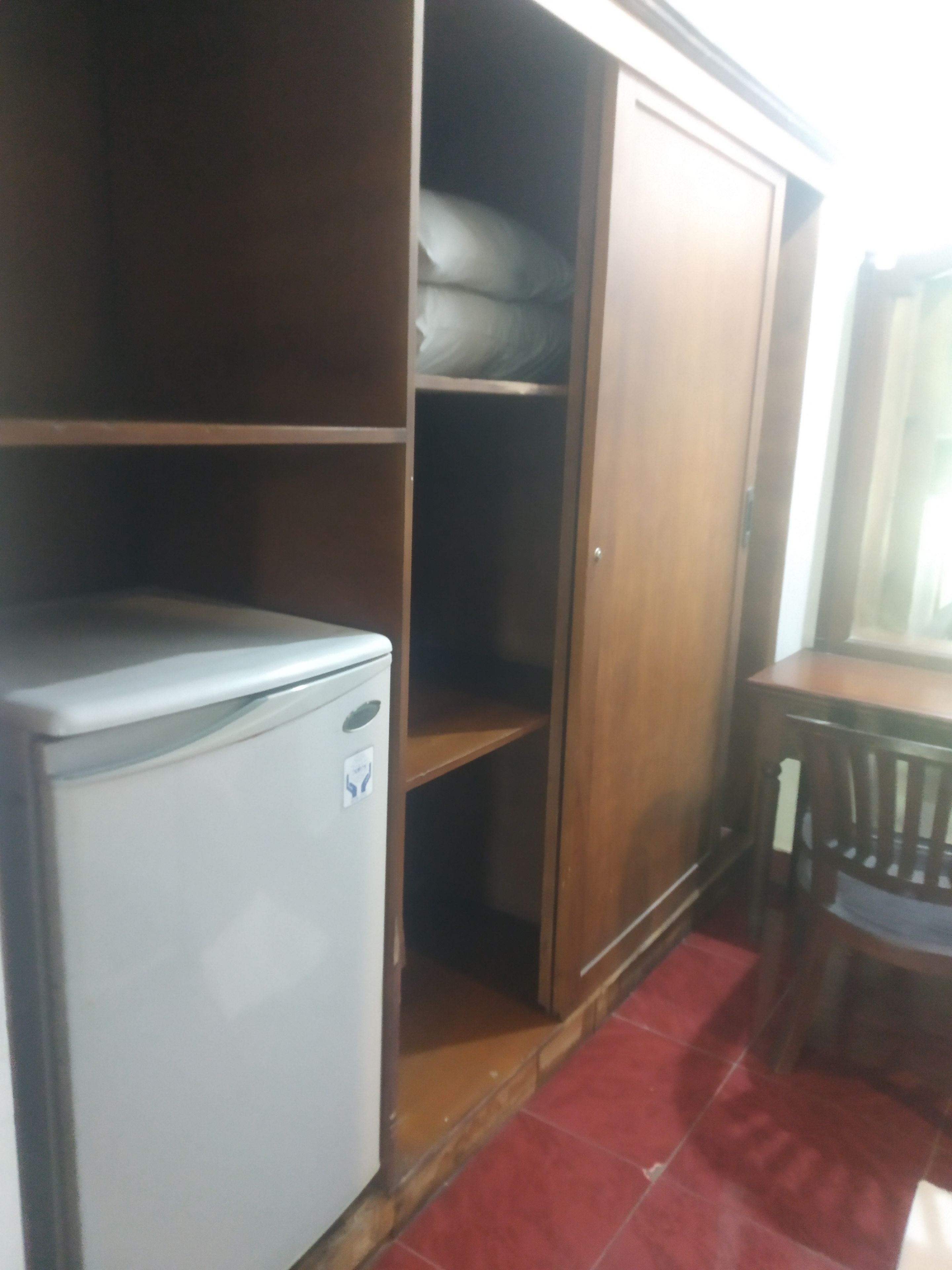 A compact room with a small refrigerator, a wooden cabinet, and a dining table with a chair.