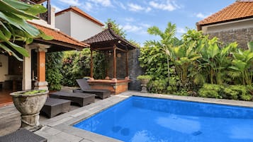 Una piscina con bordeado de baldosas, rodeada de abundante vegetación y un quiosco tradicional.