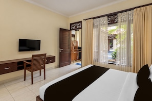 A hotel room with a bed, a desk, a chair, a television, and a view of a garden through a window with curtains.