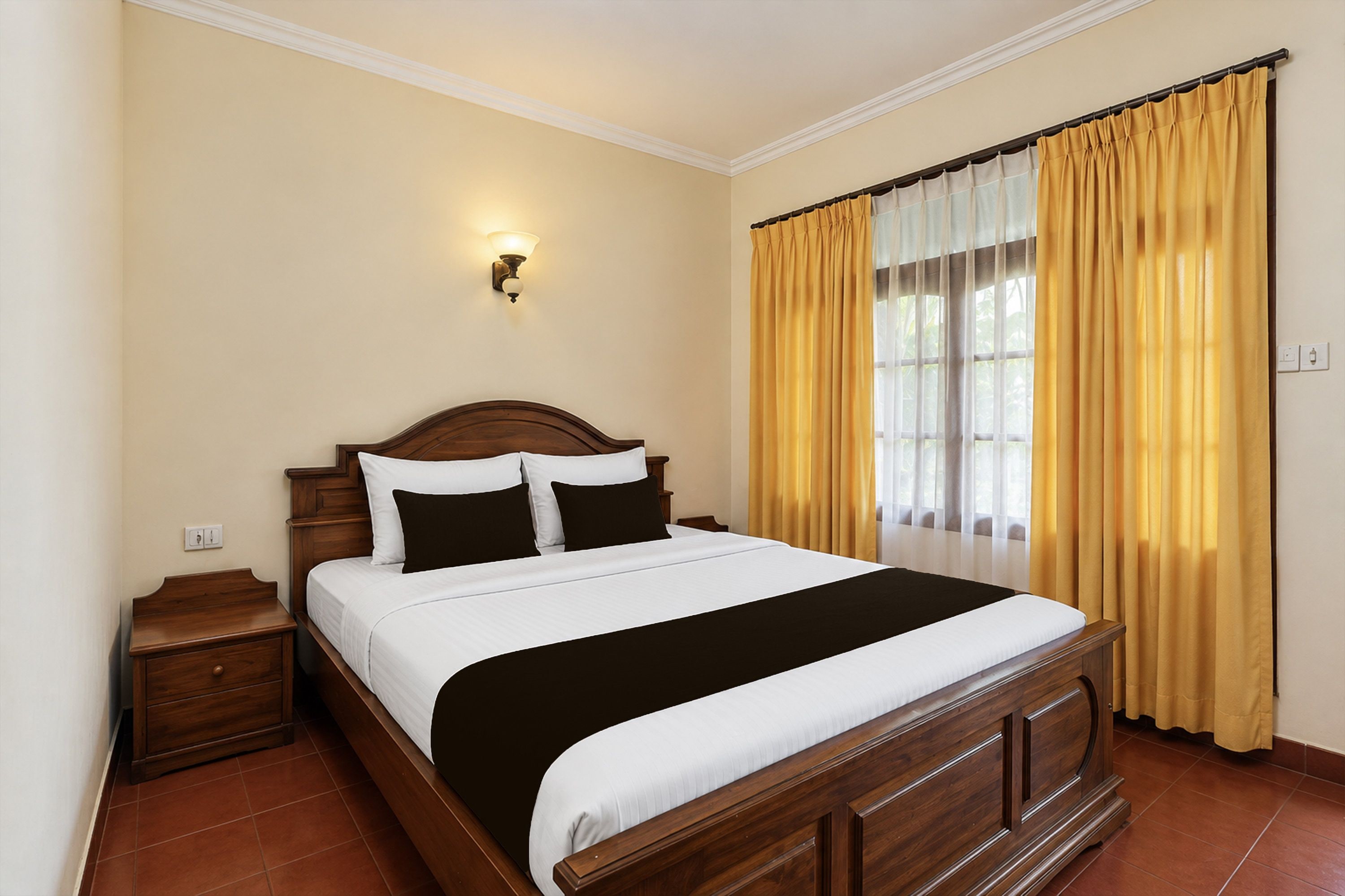 A hotel room with a wooden bed, a nightstand, a wall-mounted light, and a window with yellow curtains.