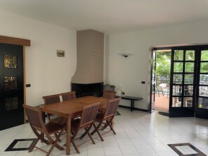 Ein Essbereich mit einem Holztisch und Stühlen, einem Kamin und Blick durch eine Glastür auf eine Terrasse.