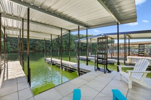 A covered outdoor area with a dock extending into a body of water, surrounded by greenery. - Lake & Leisure-Dock, Game Room, Golf Cart, (Winchester)