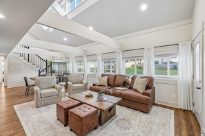 A spacious living room with a brown leather sofa, striped armchairs, a coffee table, and a staircase leading to an upper level. - Lake & Leisure-Dock, Game Room, Golf Cart, (Winchester)
