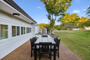 A patio with a table and chairs, a shed, and a lawn with trees. - Lake & Leisure-Dock, Game Room, Golf Cart, (Winchester)