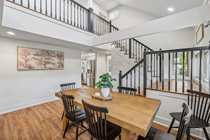 A dining area with a wooden table, black chairs, a potted plant, and a staircase with black railings. - Lake & Leisure-Dock, Game Room, Golf Cart, (Winchester)