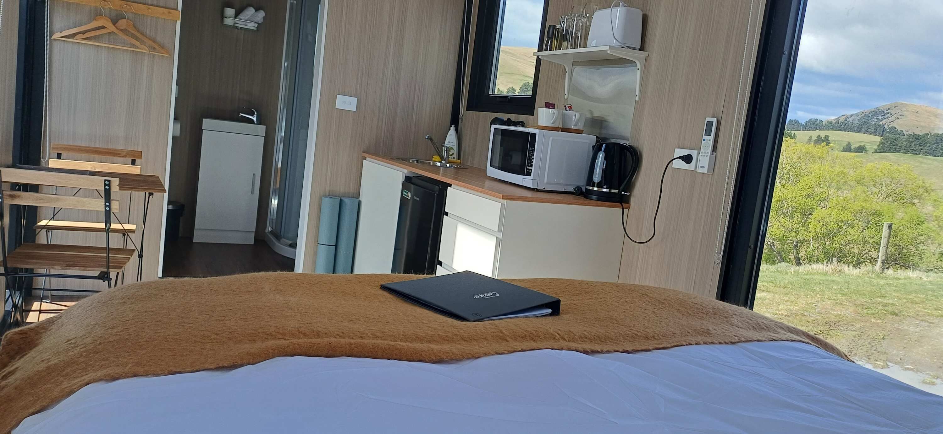 Ein Schlafzimmer mit Bett, Nachttisch, Fenster mit Blick auf die Landschaft und einer Küchenzeile mit Mikrowelle und Wasserkocher.