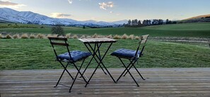 Eine Terrasse mit Holztisch und zwei Stühlen mit Blick auf ein saftiges Grasfeld und schneebedeckte Berge.