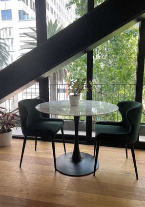 A round glass table with two chairs, a potted plant, and a view of a building and trees through large windows. - Comfortable apartment undergoing renovation in downtown Mexico City (Ciudad de México)
