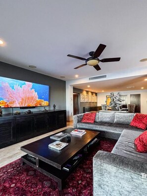 A modern living room with a flat-screen TV, a ceiling fan, and a sectional sofa with red cushions. - Casa Marvela Beachfront Penthouse 1BR (La Paz)