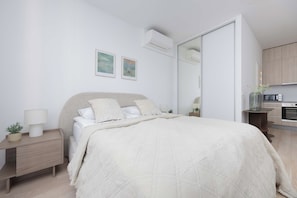Ein modernes Schlafzimmer mit einem Bett, Nachttischen, einer Nachttischlampe und einem kleinen Topf mit Pflanze.