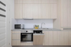 A modern kitchen with light wood cabinetry, a built-in microwave, a stainless steel sink, and a dishwasher. - Warsaw | 61 Krochmalna | Modern Studio | Air-conditioning (Warszawa)