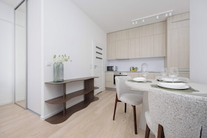 A modern kitchen with wooden cabinets, a built-in microwave, and a dining area with a table set for two. - Warsaw | 61 Krochmalna | Modern Studio | Air-conditioning (Warszawa)