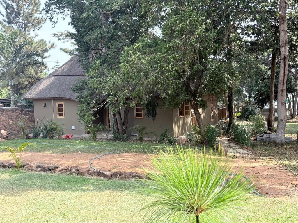 Une maison à toiture de chaume, entourée d’un jardin où poussent différentes plantes, avec un petit arbre en premier plan.
