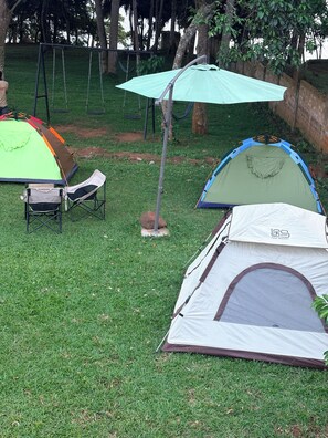 Two tents set up on a grassy lawn with a swing set and umbrella in the background.