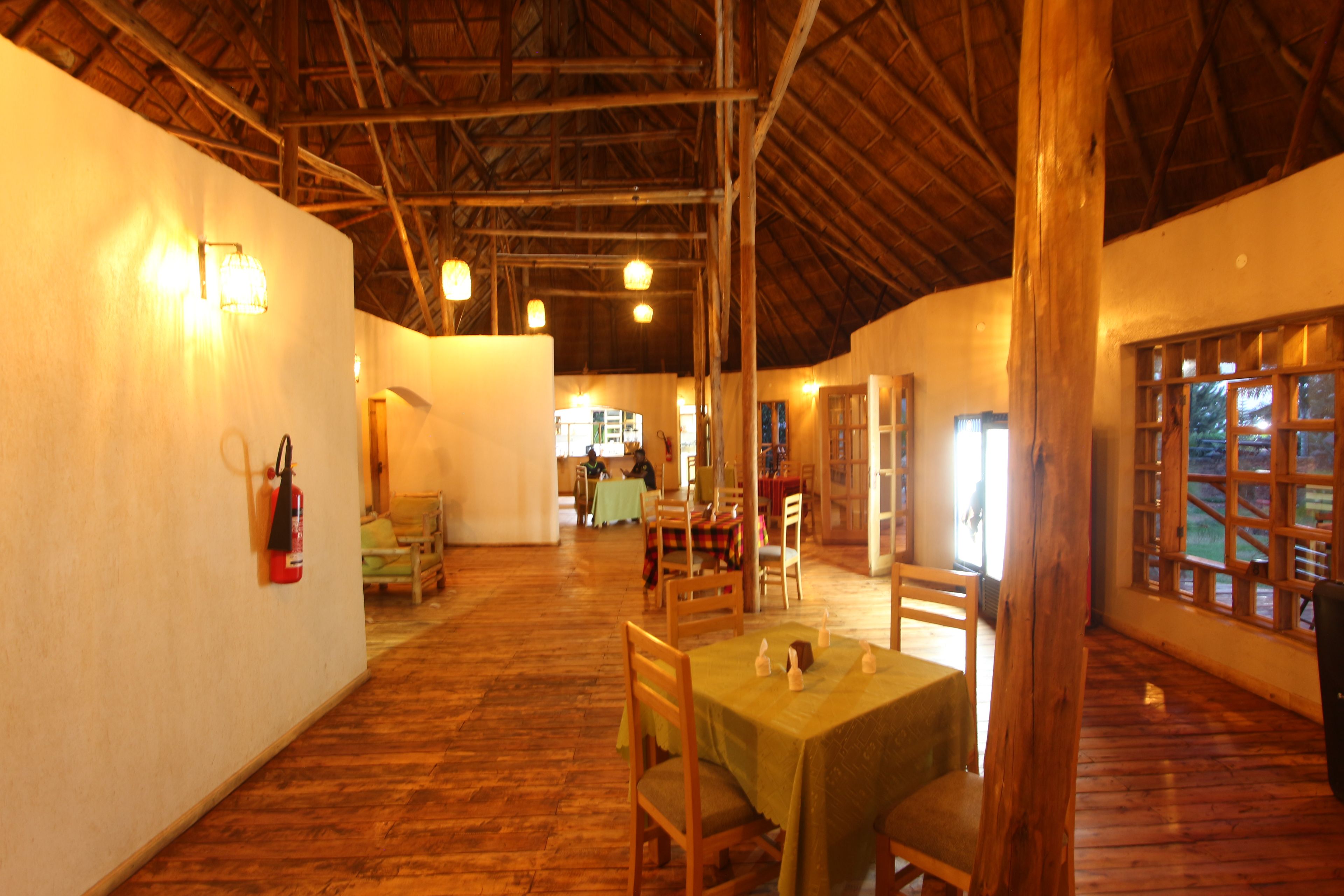 Un comedor amplio con suelos de madera y mesas, un extintor en la pared, y vistas a través de una ventana.