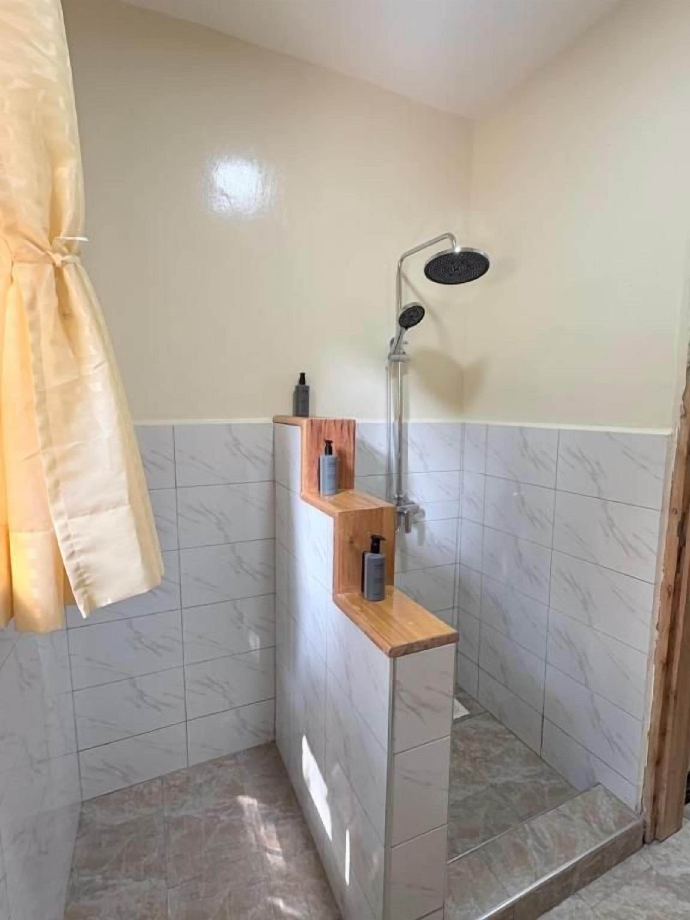 Un baño pequeño con ducha, un estante de madera con artículos de aseo y una toalla colgada en la pared.