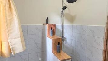 Un baño pequeño con ducha, un estante de madera con artículos de aseo y una toalla colgada en la pared.