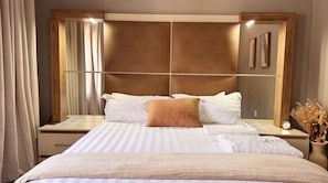 Habitación de hotel con una cama grande, un cabecero de madera, una mesita de noche con un reloj y un espejo.