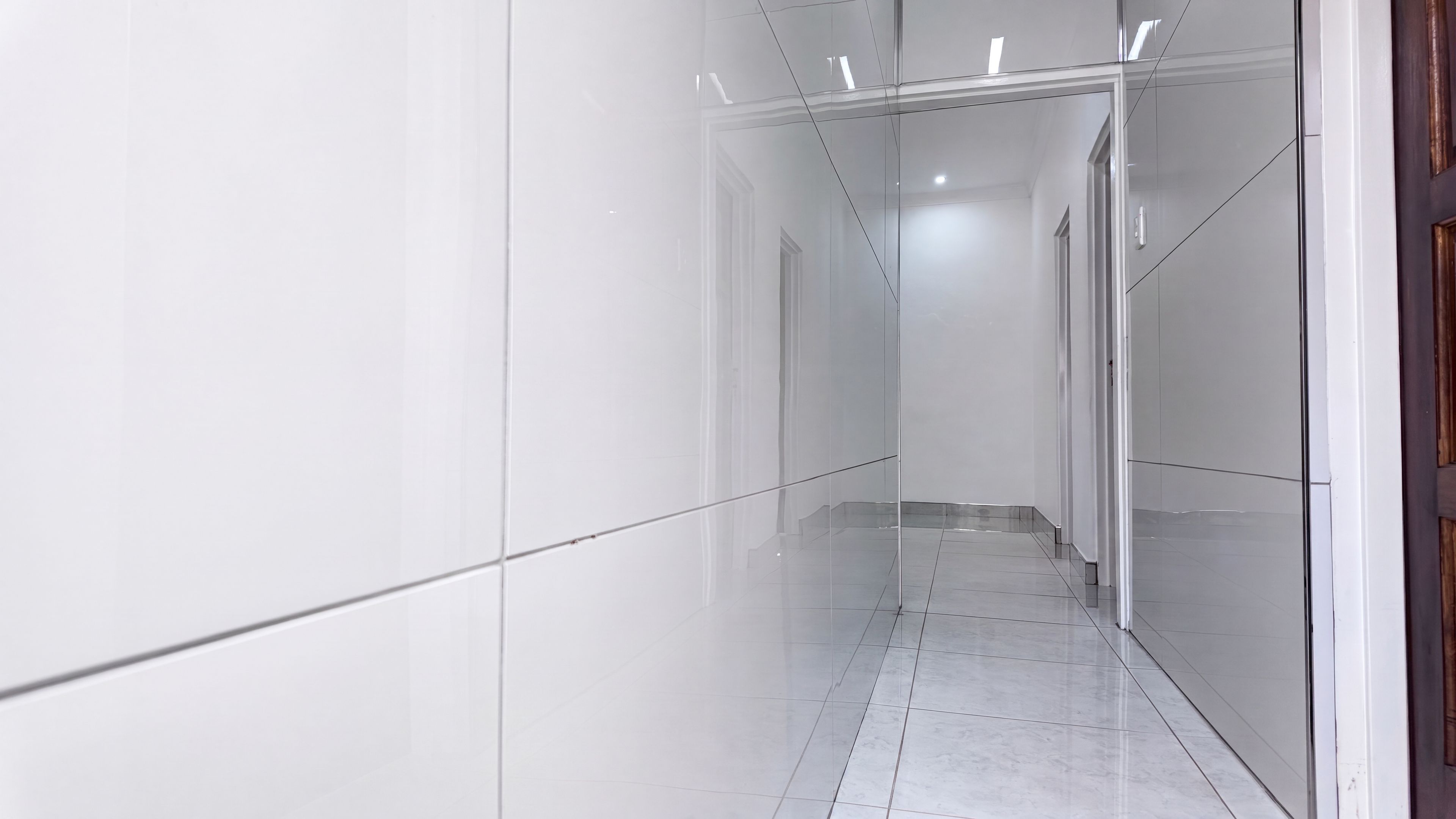 A corridor with white walls and a tiled floor, leading to a door at the end.