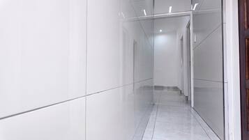 A corridor with white walls and a tiled floor, leading to a door at the end.