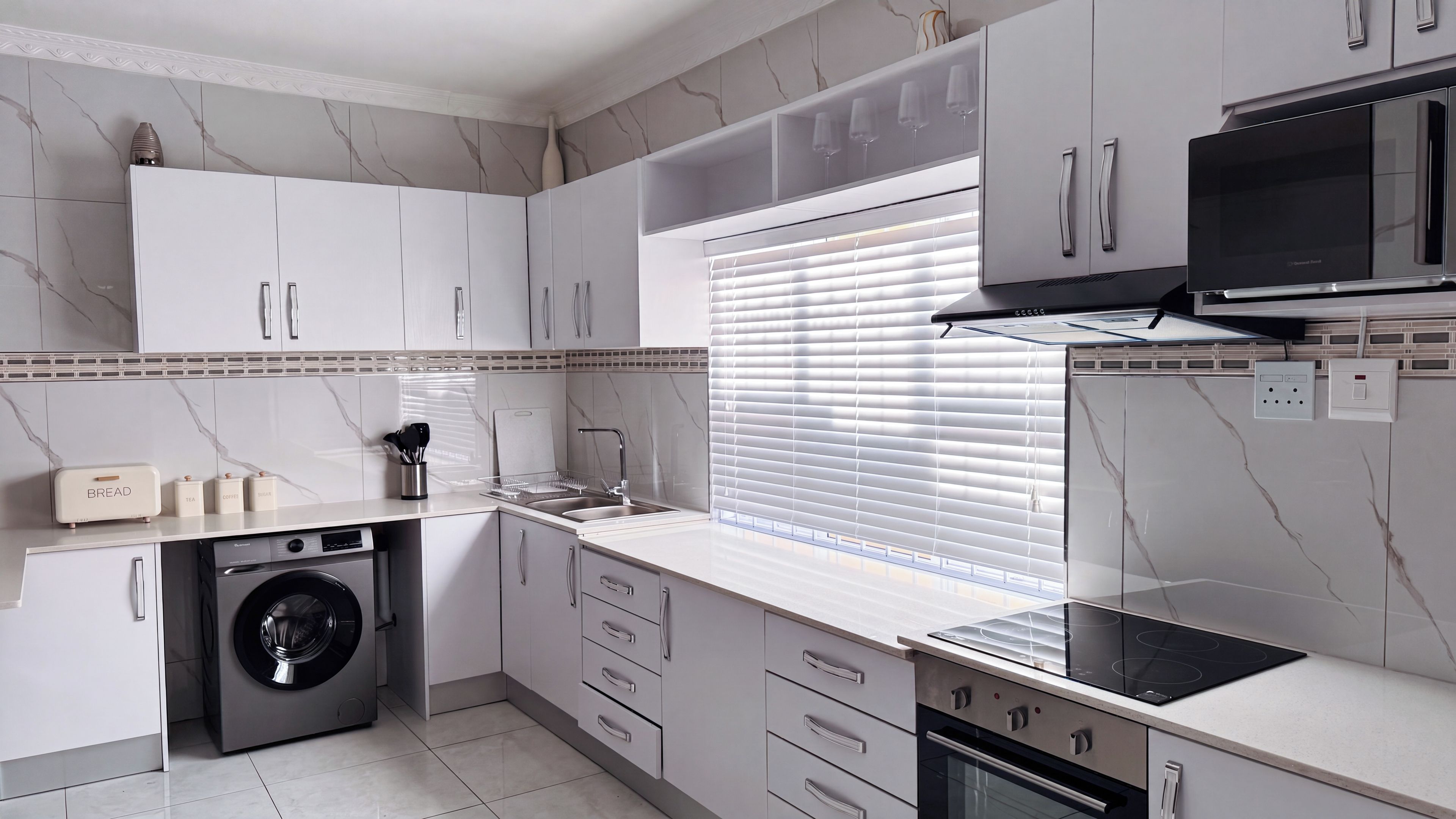A modern kitchen with white cabinetry, a built-in washing machine, a stove, and a microwave.