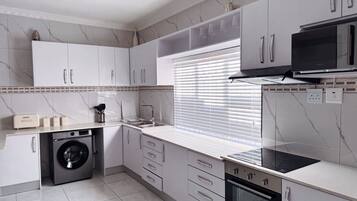 A modern kitchen with white cabinetry, a built-in washing machine, a stove, and a microwave.