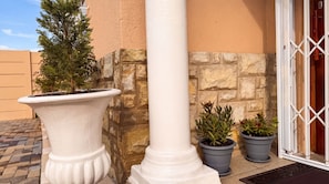 Una esquina de edificio con una columna blanca, una planta en maceta y un muro de piedra.