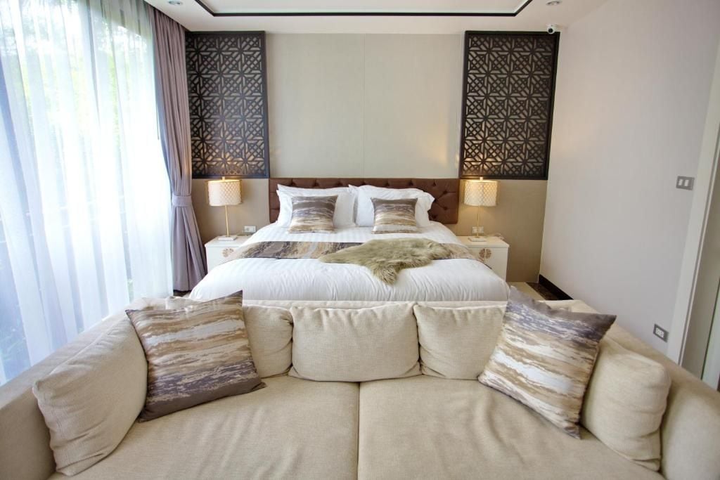 Quarto de hotel com uma cama grande, um sofá, painéis decorativos na parede e uma janela com cortinas.
