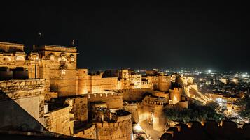 Una fortaleza histórica con múltiples torres y muros, rodeada por un paisaje urbano nocturno.