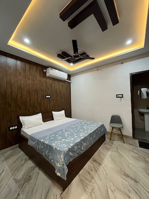 Ein Schlafzimmer mit einem Bett, einem Deckenventilator, einer Klimaanlage, einem Sessel und einem Badezimmer mit einem Waschbecken.