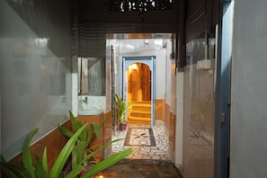 A hallway leading to a wooden door, with a bathroom on the left and a tiled floor.