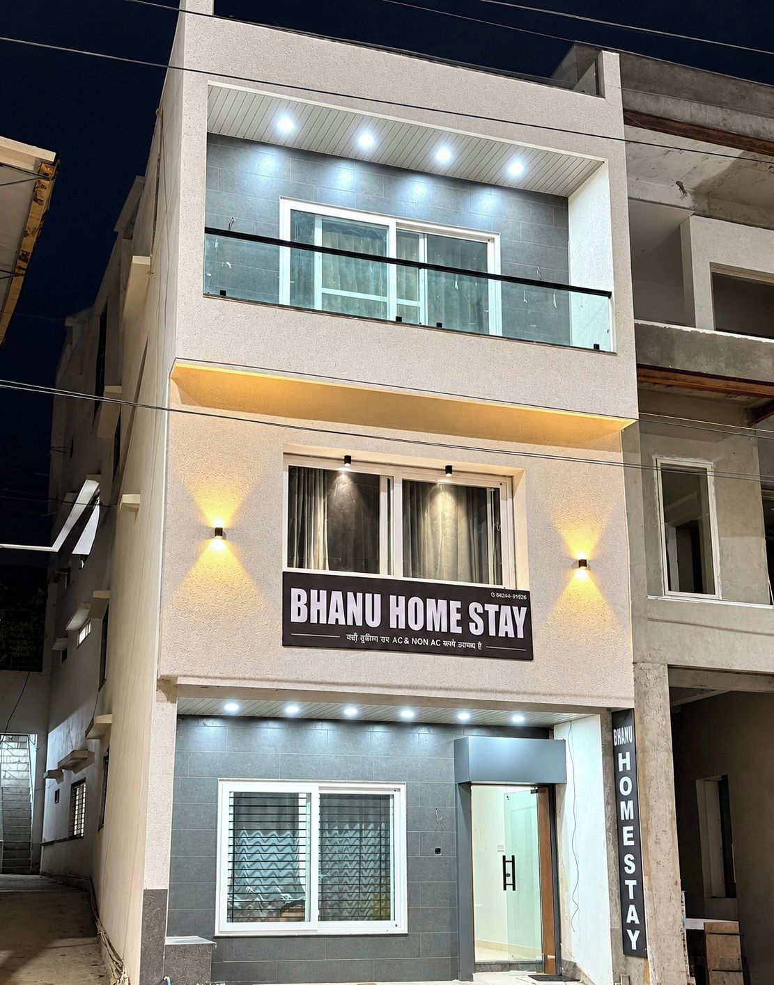 Un bâtiment à deux étages, avec une enseigne indiquant « BHANU HOME STAY » et une porte d’entrée bien visible.